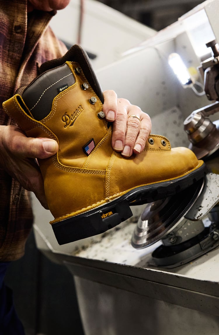 A holds up a pair of brown work boots in a factory