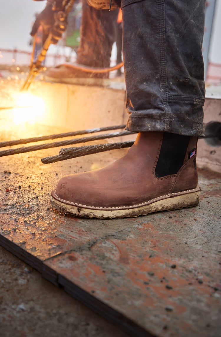 A holds up a pair of brown work boots in a factory