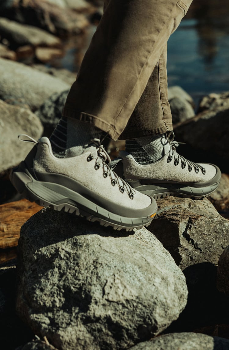 A man hiking through an open field with rocks in the background