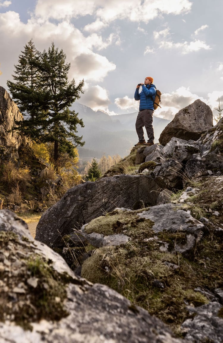 A man hiking through an open field with rocks in the background