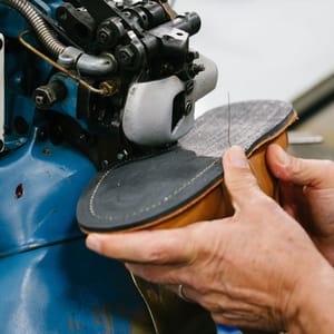 A muted brown leather boot shown in profile view with dirt smudges on the light gray midsole and side of the boot.