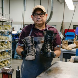 A brown leather boot shown in profile view with teal textile inlays and gold eyelets, there is some dirt showing on the outsole.