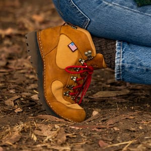 A brown leather boot shown in profile view with yellow textile inlays, there are dirt smudges on the toe and sides of the boot.