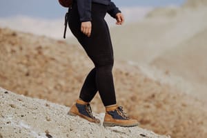 a man hikes against the backdrop of alpine lake wearing brown and red hiking boots
