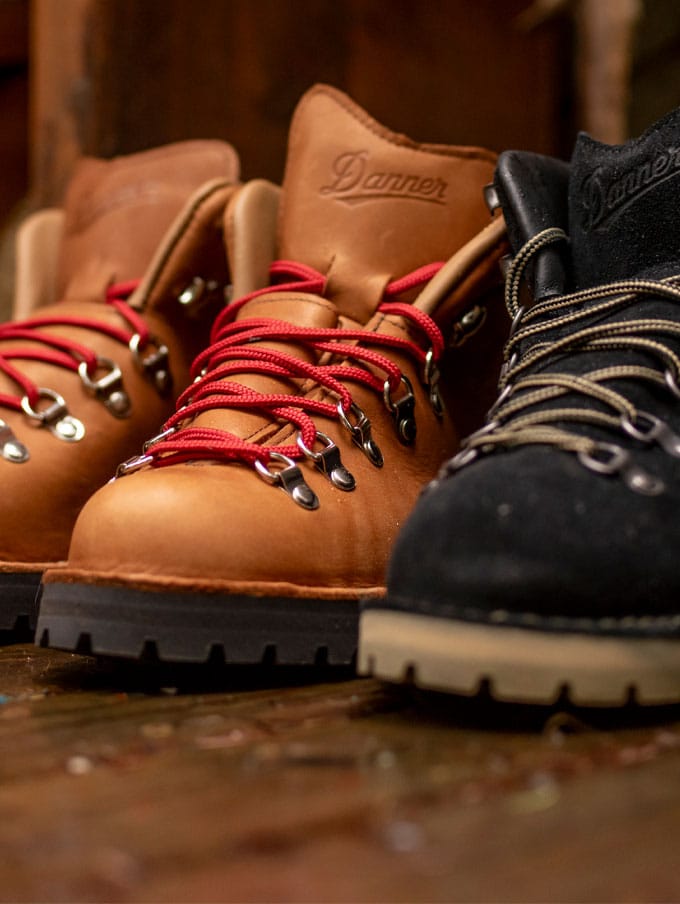 A hiker climbs rocky terrain with clouds and trees visible in the background below