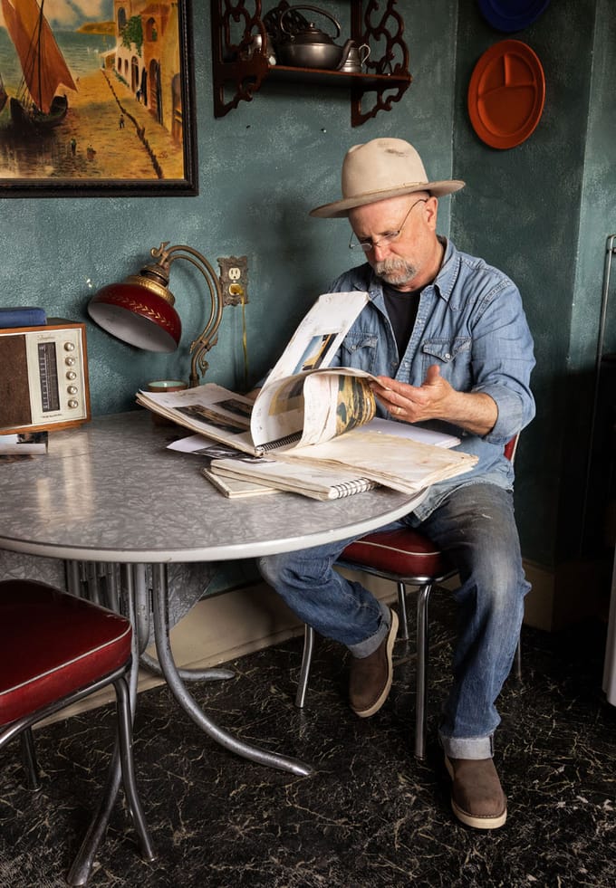 a man sits at a table looking through collections of art