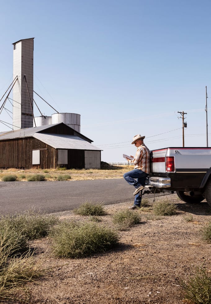 a man sketches while leaning against the back of his truck