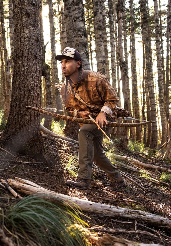 A man with a bow and arrow stalks in the woods