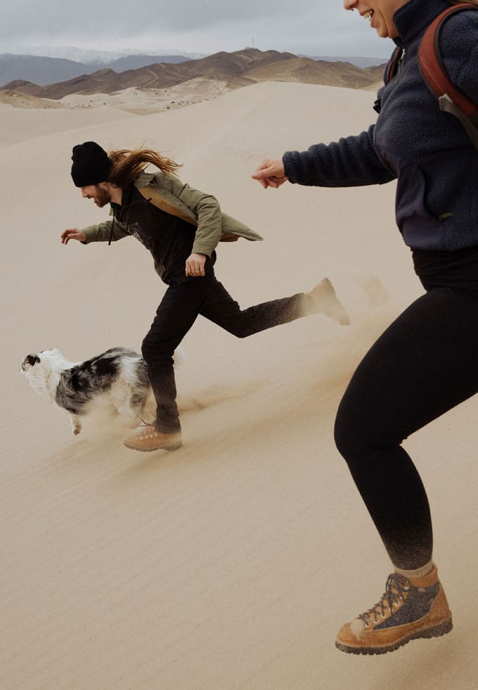 two people and a dog running down a sandy dune