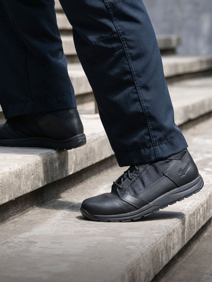 A person walks briskly up a metal staircase wearing polished black leather uniform boots and black pants