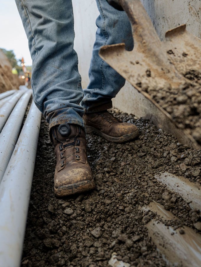 a worker climbs into a backhoe while wearing brown work boots