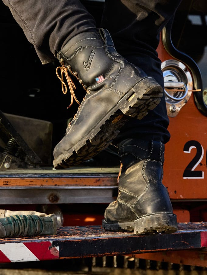 a worker climbs into a backhoe while wearing brown work boots