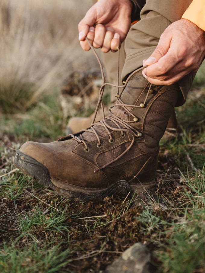 A hunter adorned in camo carries his rifle up a steep rocky hill