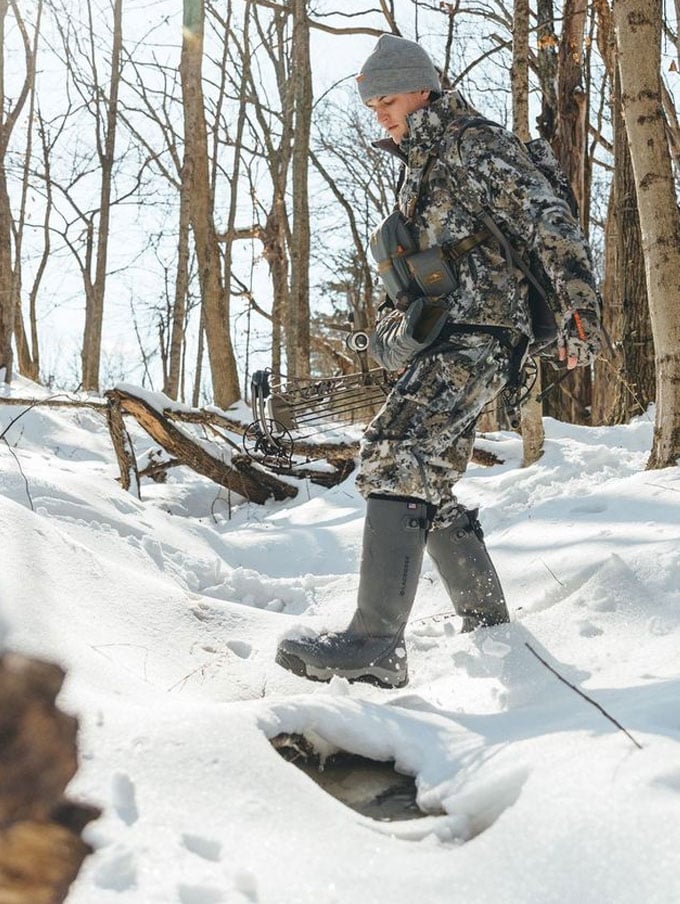 a man sits in the back of his truck adorned in camo and wearing knee high rubber boots