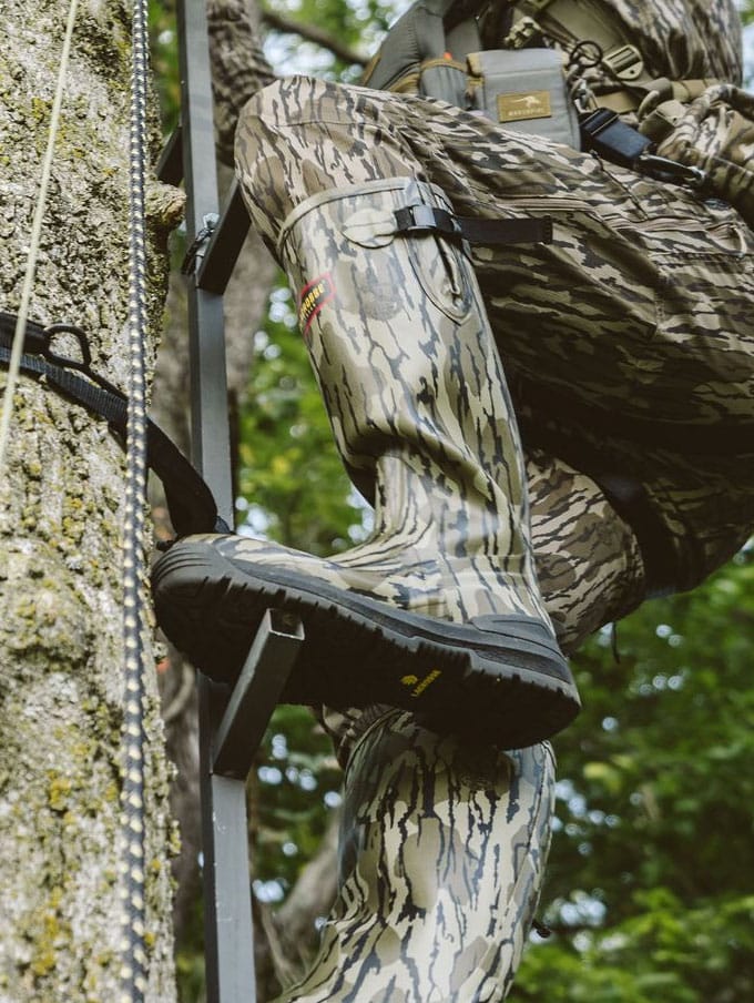 a man sits in the back of his truck adorned in camo and wearing knee high rubber boots