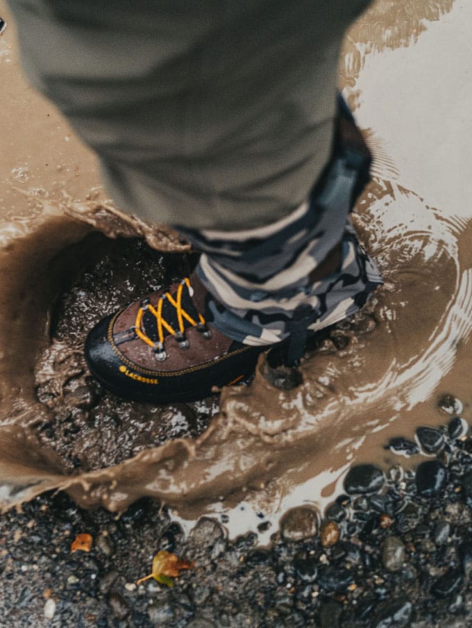a man in a camo jacket walks through a stream while wearing brown leather hunting boots with a black rubber rand