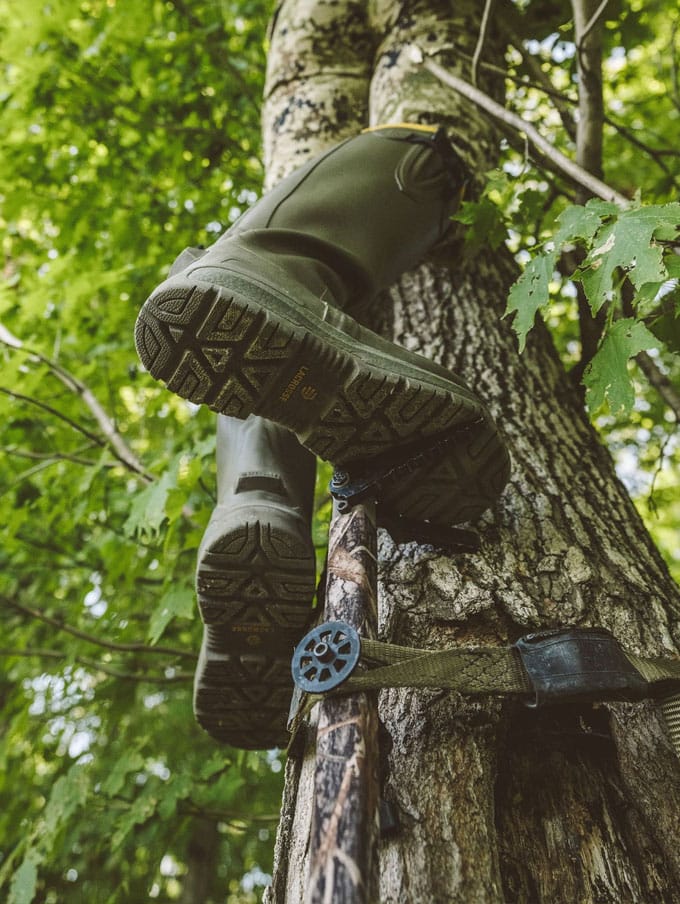a man sits in the back of his truck adorned in camo and wearing knee high rubber boots