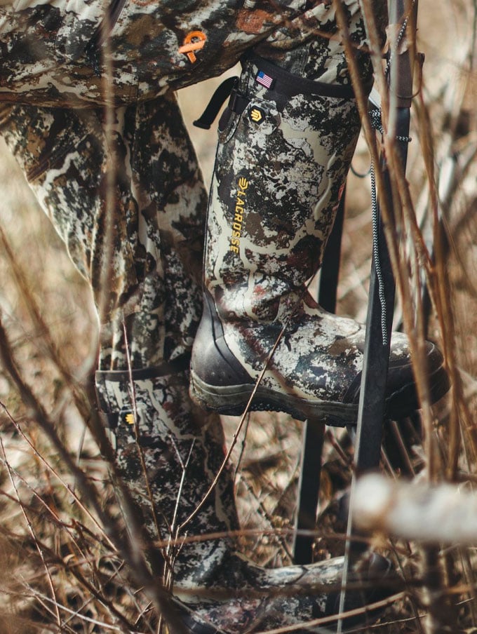 a man sits in the back of his truck adorned in camo and wearing knee high rubber boots