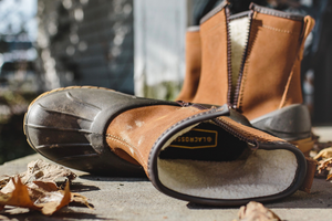 A brown leather boot shown in profile view with teal textile inlays and gold eyelets, there is some dirt showing on the outsole.