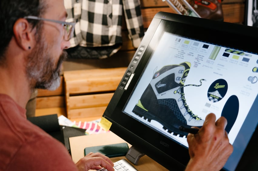 A man is using a computer to design a pair of Danner Boots.
